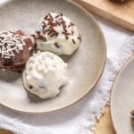 Creamy ice cream scoops with chocolate and vanilla toppings on a beige ceramic plate, served on a wooden table with a white fringed cloth, perfect for dessert recipes and sweet treats.
