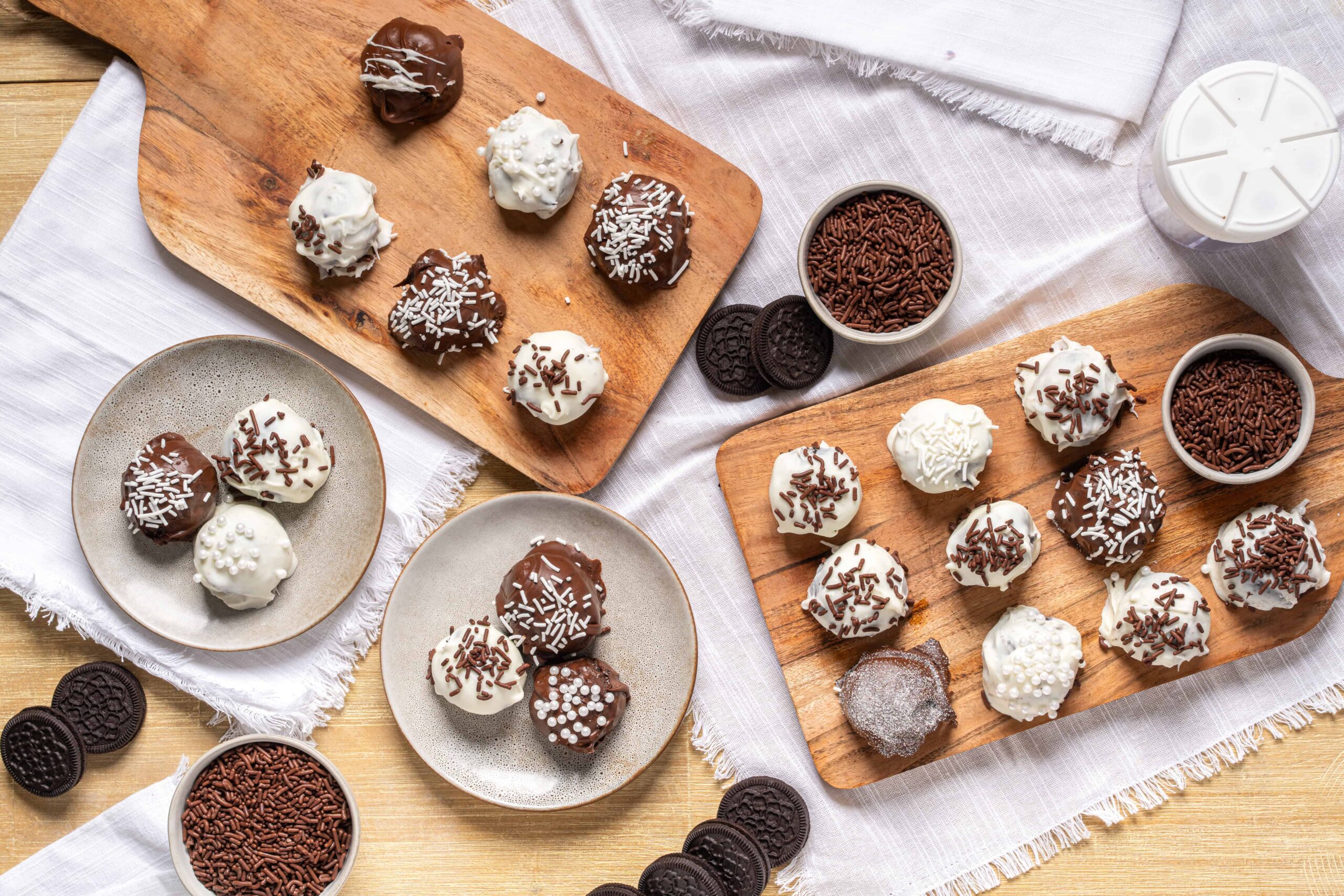 Rich chocolate truffles topped with sprinkles and cocoa powder, served on wooden and ceramic plates with chocolate sprinkles and cookies for a delicious dessert treat.