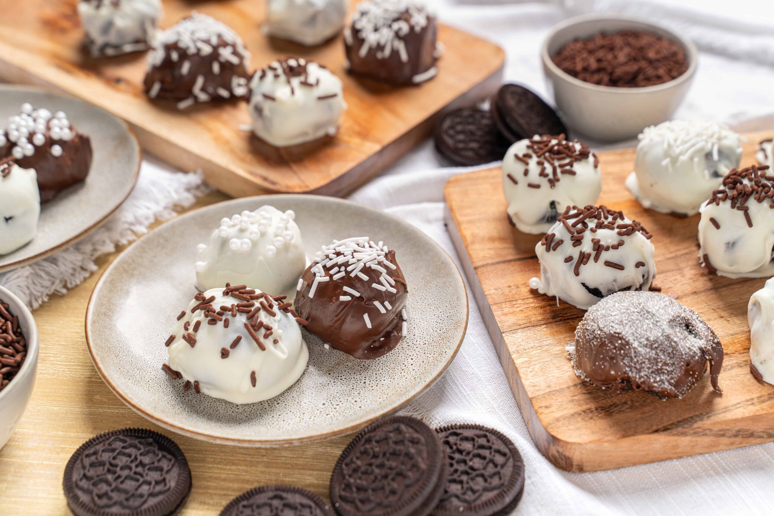 Cream cheese Oreo balls dipped in white and milk chocolate with sprinkles on a ceramic plate and wooden boards, delicious Oreo dessert, easy Oreo truffles, chocolate-covered Oreo treat, no-bake Oreo snack.