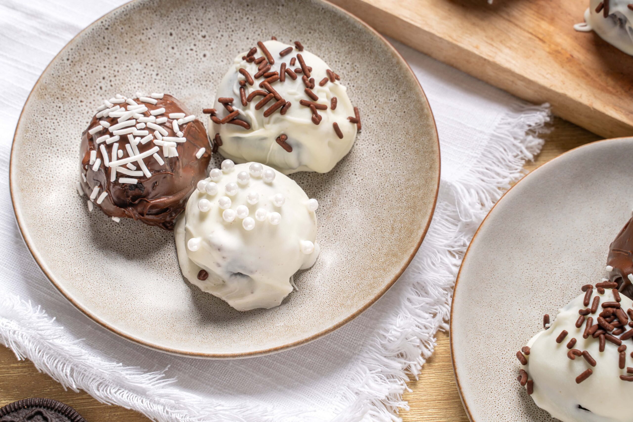 Creamy ice cream scoops with chocolate and vanilla toppings on a beige ceramic plate, served on a wooden table with a white fringed cloth, perfect for dessert recipes and sweet treats.