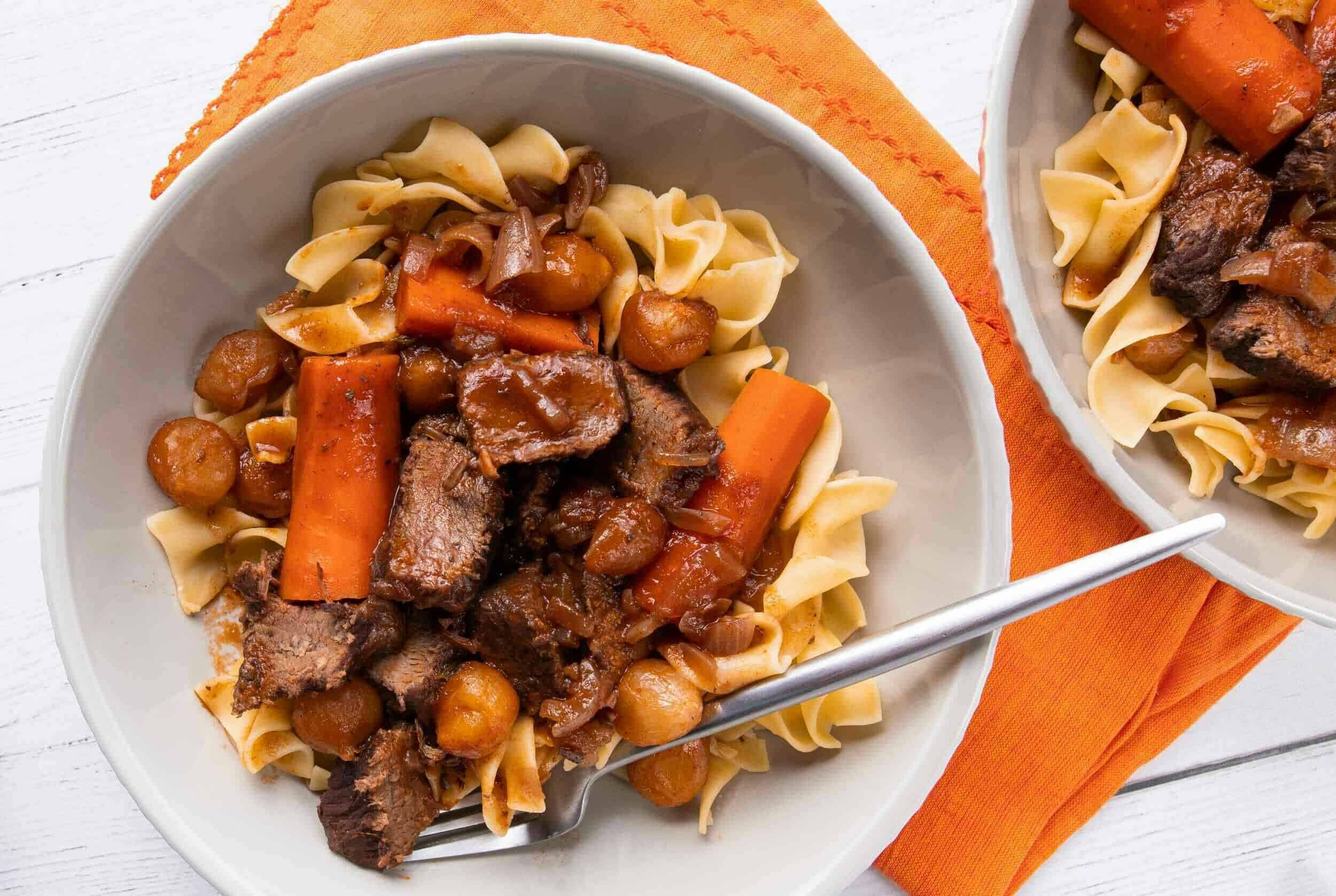 Slow cooker beef stew with carrots, potatoes, and tender beef chunks served over egg noodles, perfect for hearty comfort food meals.