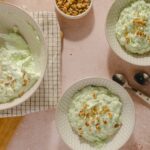 Creamy cucumber salad with chopped nuts garnished with crushed peanuts, served in decorative bowls on a pink countertop.