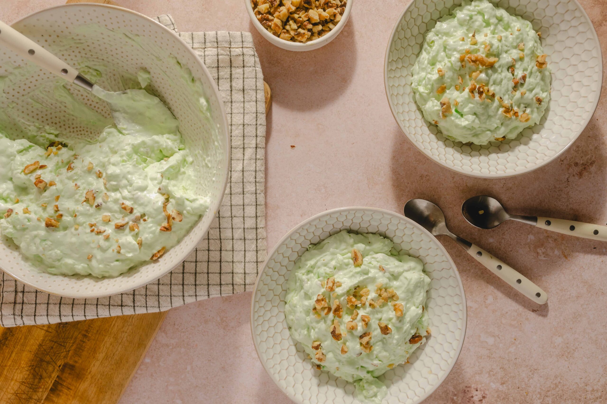 Creamy cucumber salad with chopped nuts garnished with crushed peanuts, served in decorative bowls on a pink countertop.