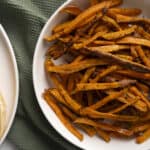 Crispy roasted sweet potato fries on white plate, healthy vegetable snack, baked sweet potato strips, side dish for meals, delicious and nutritious sweet potato fries alt text.