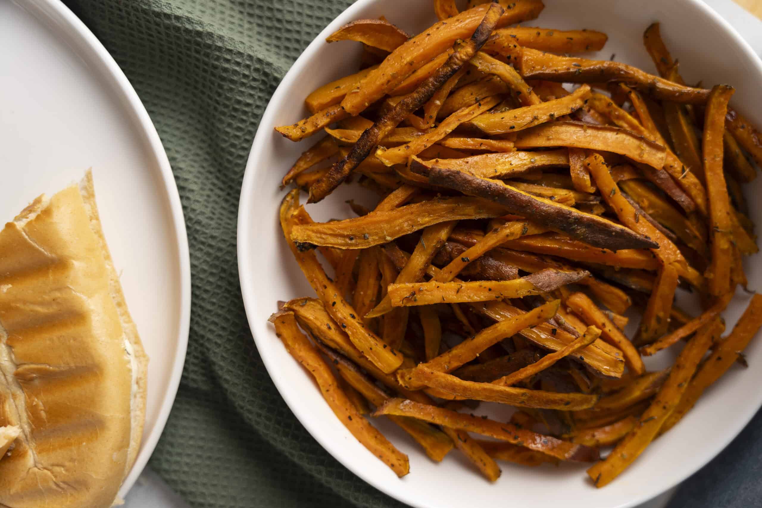 Crispy roasted sweet potato fries on white plate, healthy vegetable snack, baked sweet potato strips, side dish for meals, delicious and nutritious sweet potato fries alt text.