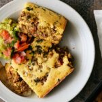 Savory baked casserole with ground beef, potatoes, and herbs served with fresh guacamole and pico de gallo. Perfect comfort food for family dinners or casual gatherings.