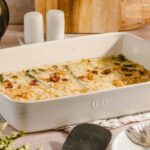 Baked vegetable and cheese casserole in a white ceramic dish, ready for serving, with herbs on top, shown on a rustic kitchen table, perfect for comfort food recipes.