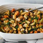 Roasted vegetable medley with Brussels sprouts, sweet potatoes, carrots, and cauliflower in a white ceramic baking dish. Fresh parsley garnish adds color and flavor.