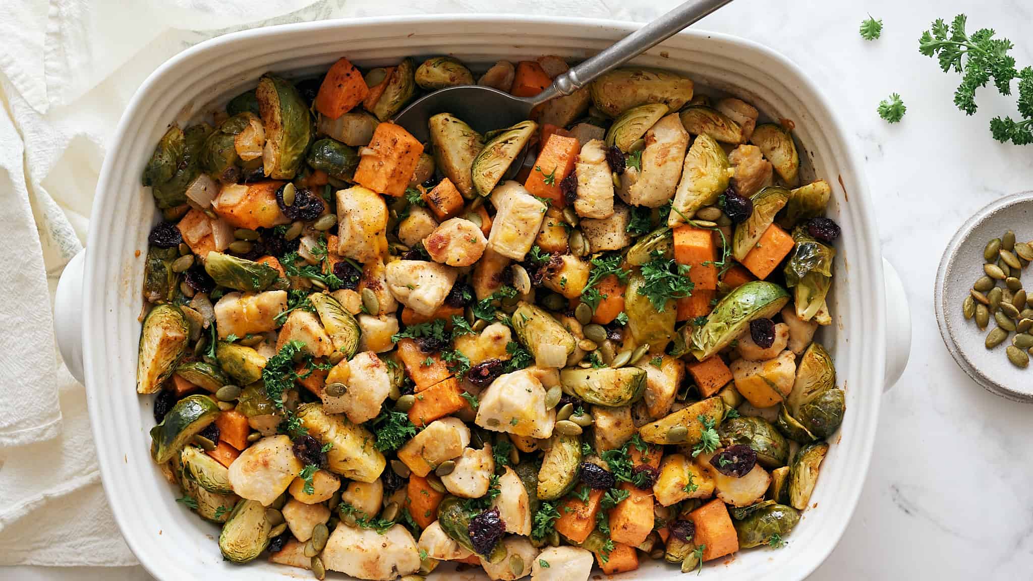 Oven-roasted vegetable medley with Brussels sprouts, sweet potatoes, cauliflower, and herbs in a white baking dish. Perfect healthy side dish for dinner or meal prep.
