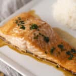 Juicy baked salmon fillet with garlic herb butter sauce, served with a side of steamed rice, garnished with fresh parsley. Perfect for healthy dinner or meal prep.