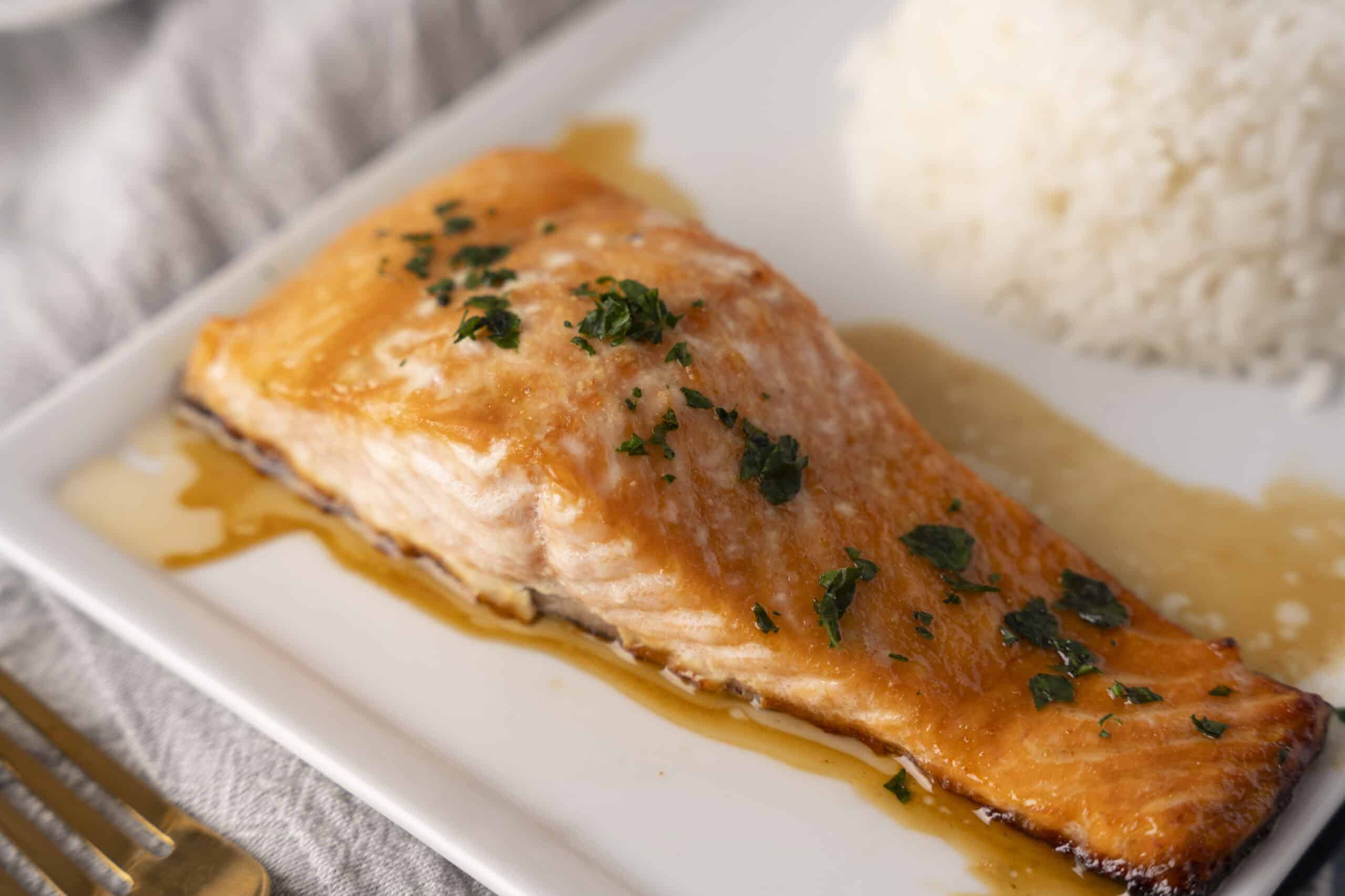 Juicy baked salmon fillet with garlic herb butter sauce, served with a side of steamed rice, garnished with fresh parsley. Perfect for healthy dinner or meal prep.
