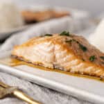Juicy baked salmon fillet garnished with herbs, served with a side of steamed rice, on a white plate. Perfect for healthy dinner recipes and seafood lovers.