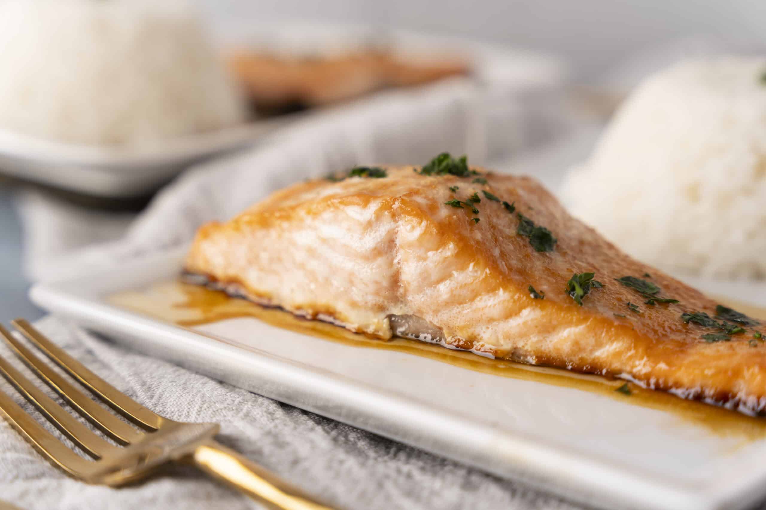 Juicy baked salmon fillet garnished with herbs, served with a side of steamed rice, on a white plate. Perfect for healthy dinner recipes and seafood lovers.
