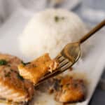 Juicy baked chicken thigh with herbs served with steamed white rice on a white plate.