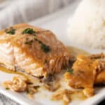 Baked salmon fillet with cheese and herbs served with a side of fluffy white rice on a white plate.