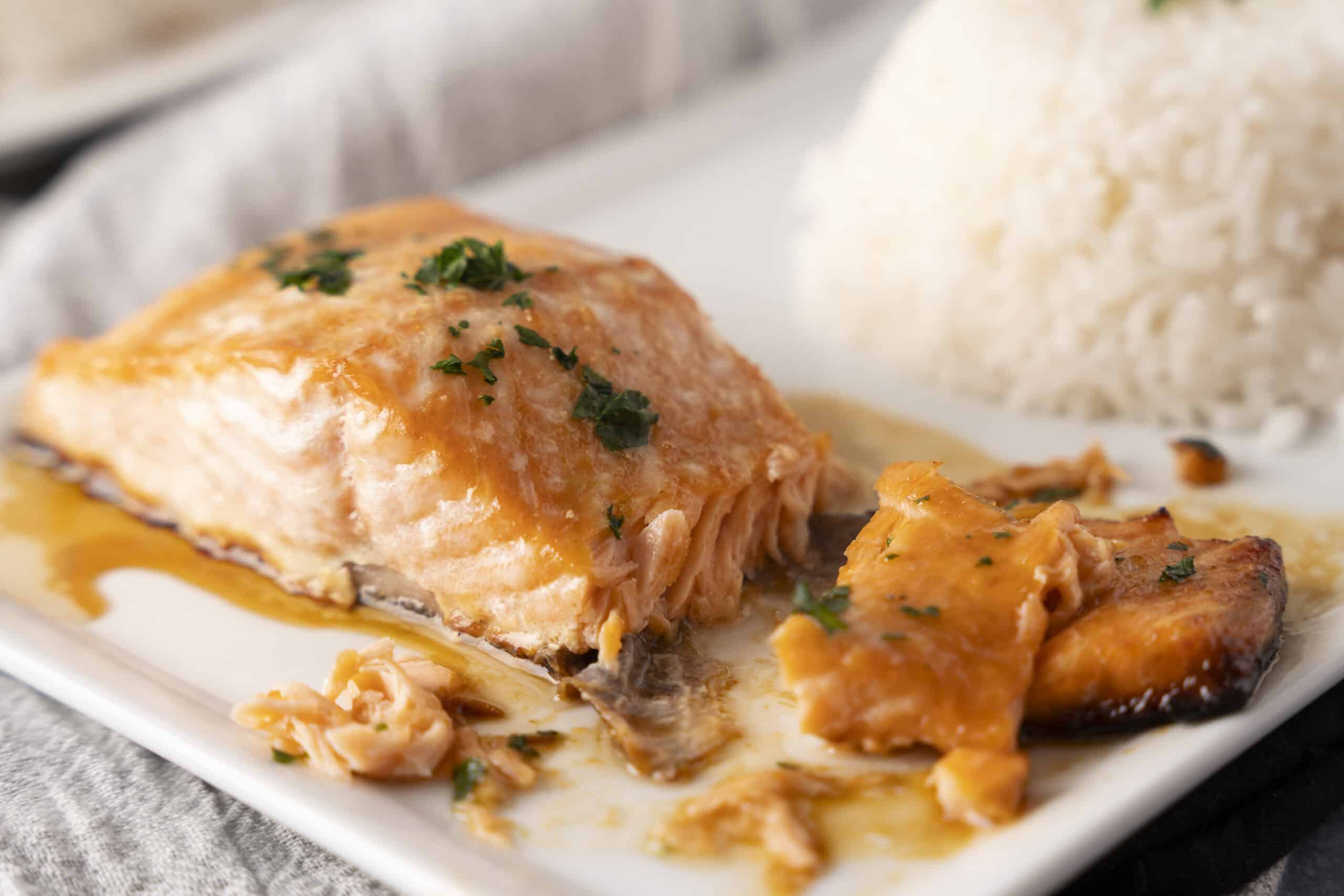 Baked salmon fillet with cheese and herbs served with a side of fluffy white rice on a white plate.