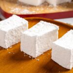 Fluffy white marshmallows on a wooden serving platter, perfect for hot chocolate or desserts. Freshly made, soft, and coated with fine powdered sugar for sweet indulgence.