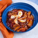 Savory peach cobbler served in a blue bowl topped with fresh peach slices, caramelized crust, and a sweet glaze, perfect for dessert or summer gatherings.
