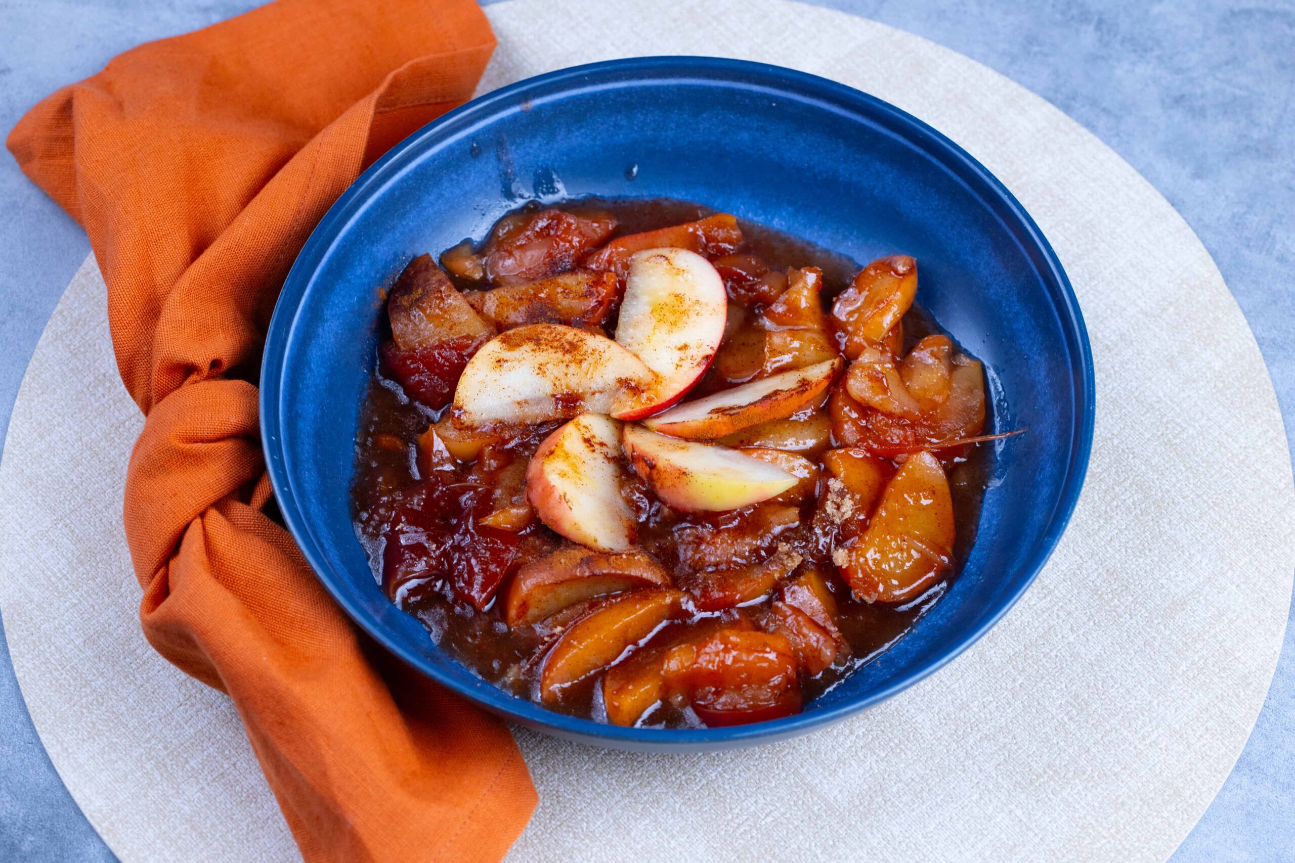 Savory peach cobbler served in a blue bowl topped with fresh peach slices, caramelized crust, and a sweet glaze, perfect for dessert or summer gatherings.
