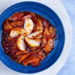 Stewed apples with cinnamon and syrup in a blue bowl, fresh fruit dessert, home-cooked apple or fruit compote, healthy sweet treat, comforting fruit dish.