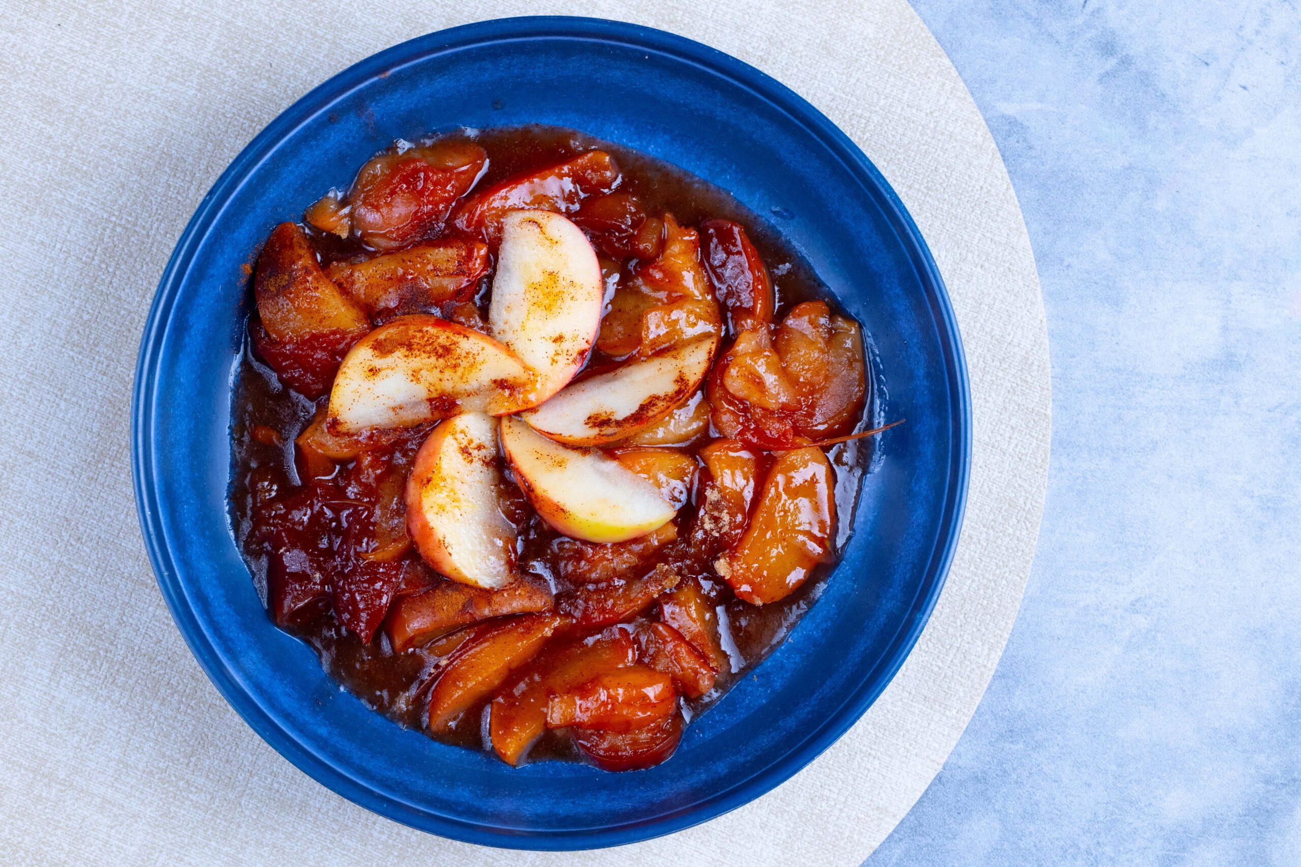 Stewed apples with cinnamon and syrup in a blue bowl, fresh fruit dessert, home-cooked apple or fruit compote, healthy sweet treat, comforting fruit dish.
