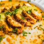 Savory chicken curry with fresh herbs and creamy sauce on a white plate, served with a sprinkle of cilantro and green onions for flavor.