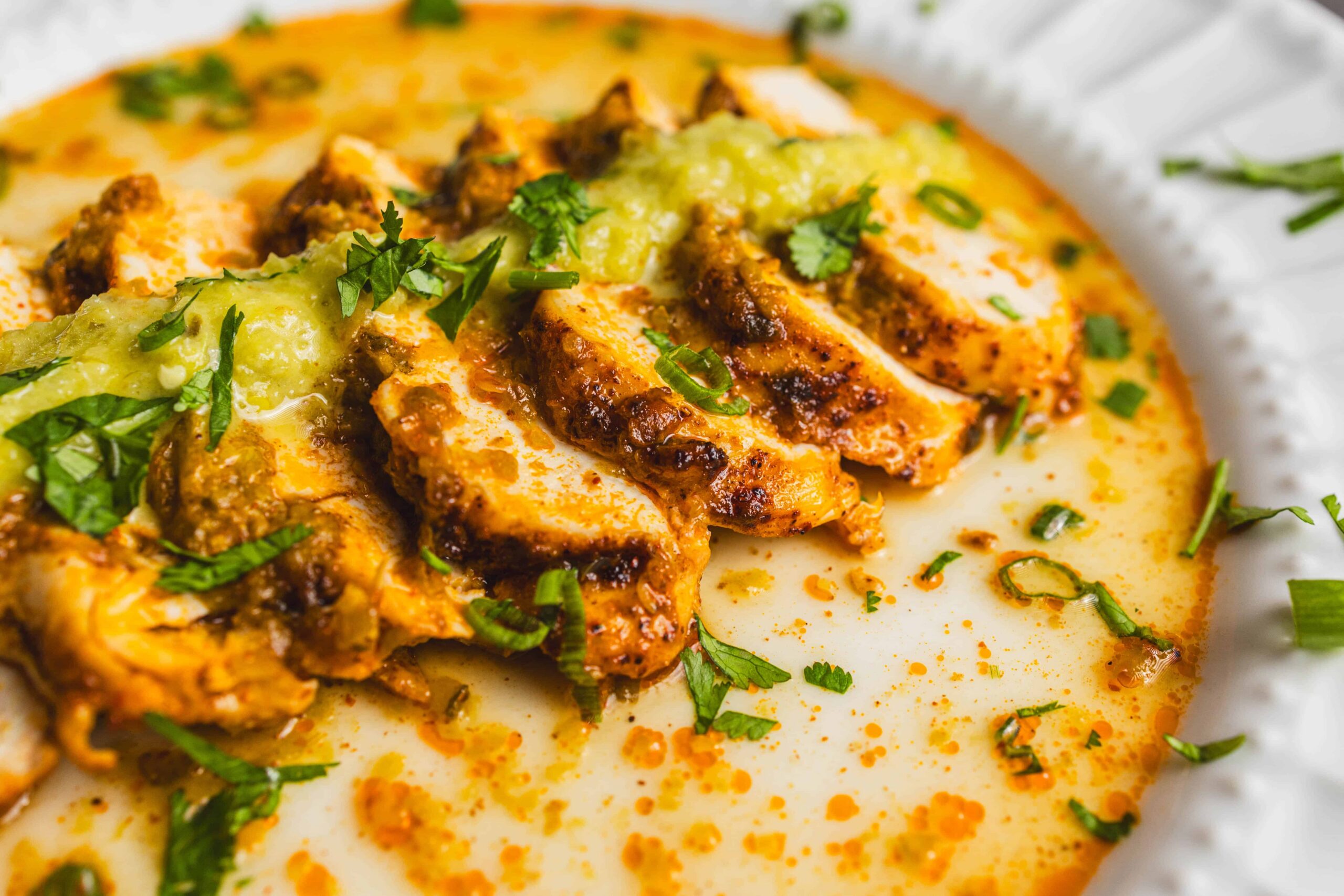 Savory chicken curry with fresh herbs and creamy sauce on a white plate, served with a sprinkle of cilantro and green onions for flavor.