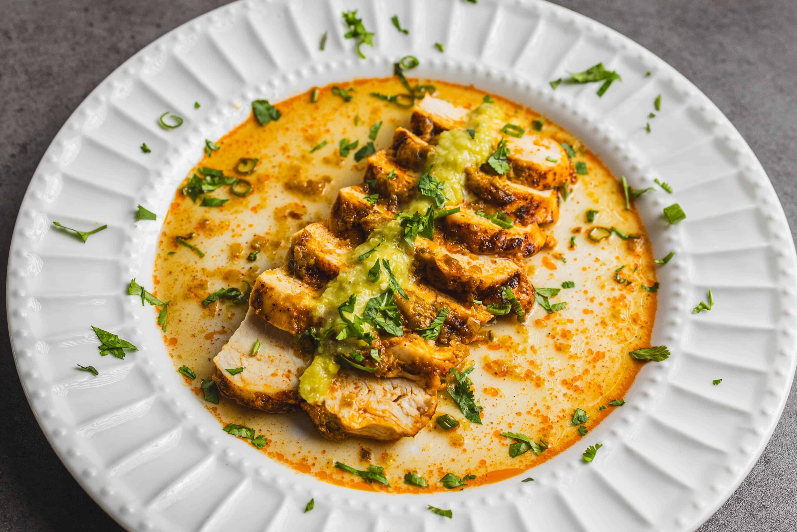Creamy chicken curry with herbs and spices served on a white decorative plate, garnished with fresh cilantro and green onions.