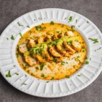 Tender grilled chicken slices topped with creamy curry sauce, garnished with fresh cilantro and green onions on a white plate. Perfect for a flavorful dinner or lunch.