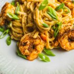 Succulent shrimp and fettuccine pasta in a savory seasoned sauce topped with fresh green onions on a stylish white plate. Perfect for a quick, delicious dinner option.