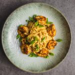 Creamy pasta with grilled shrimp and chopped green onions served on a rustic ceramic plate, perfect for seafood and pasta lovers.