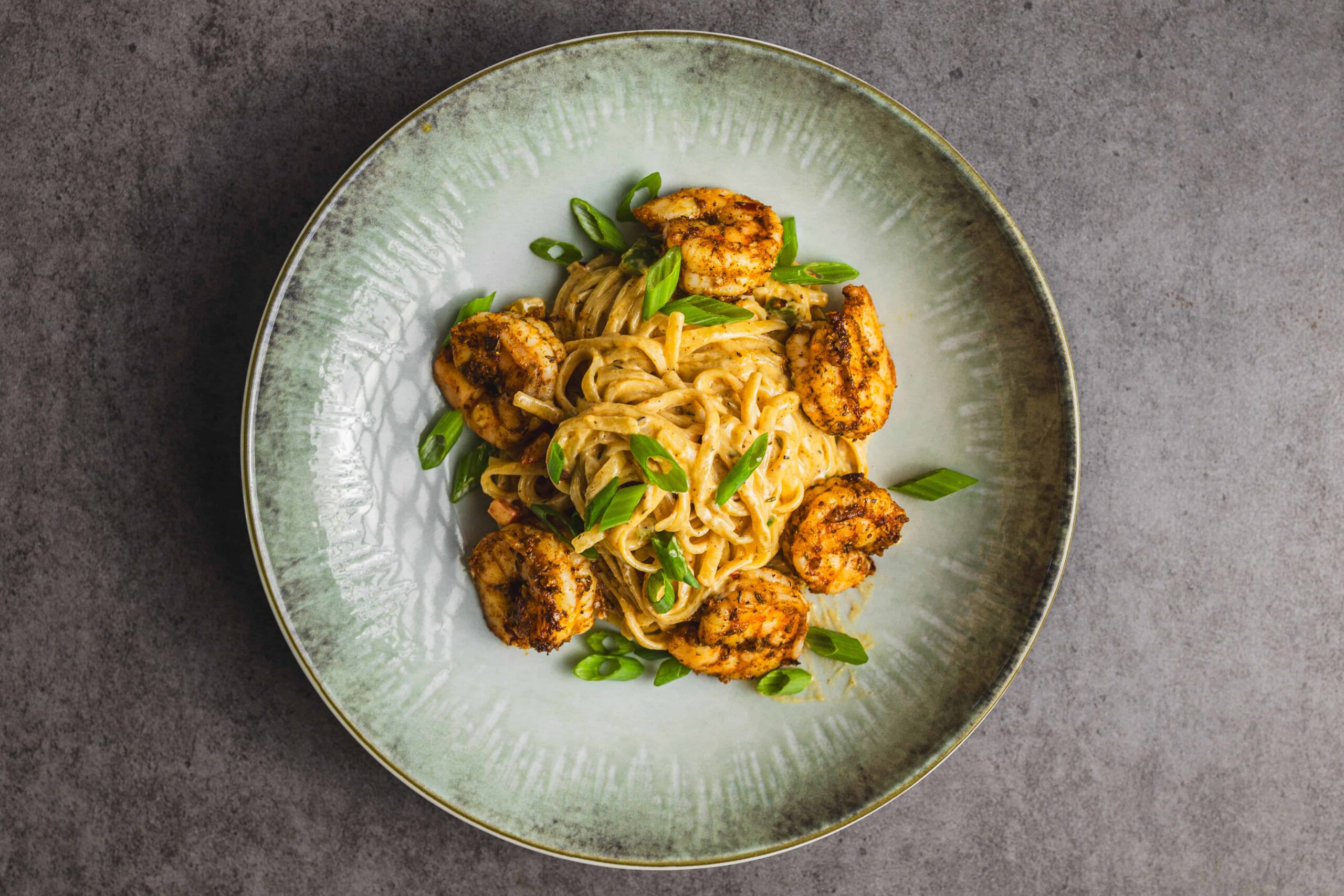 Creamy pasta with grilled shrimp and chopped green onions served on a rustic ceramic plate, perfect for seafood and pasta lovers.