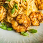 Juicy shrimp with spicy seasoning served with creamy pasta and garnished with chopped green onions, creating a delicious seafood pasta dish perfect for dinner.
