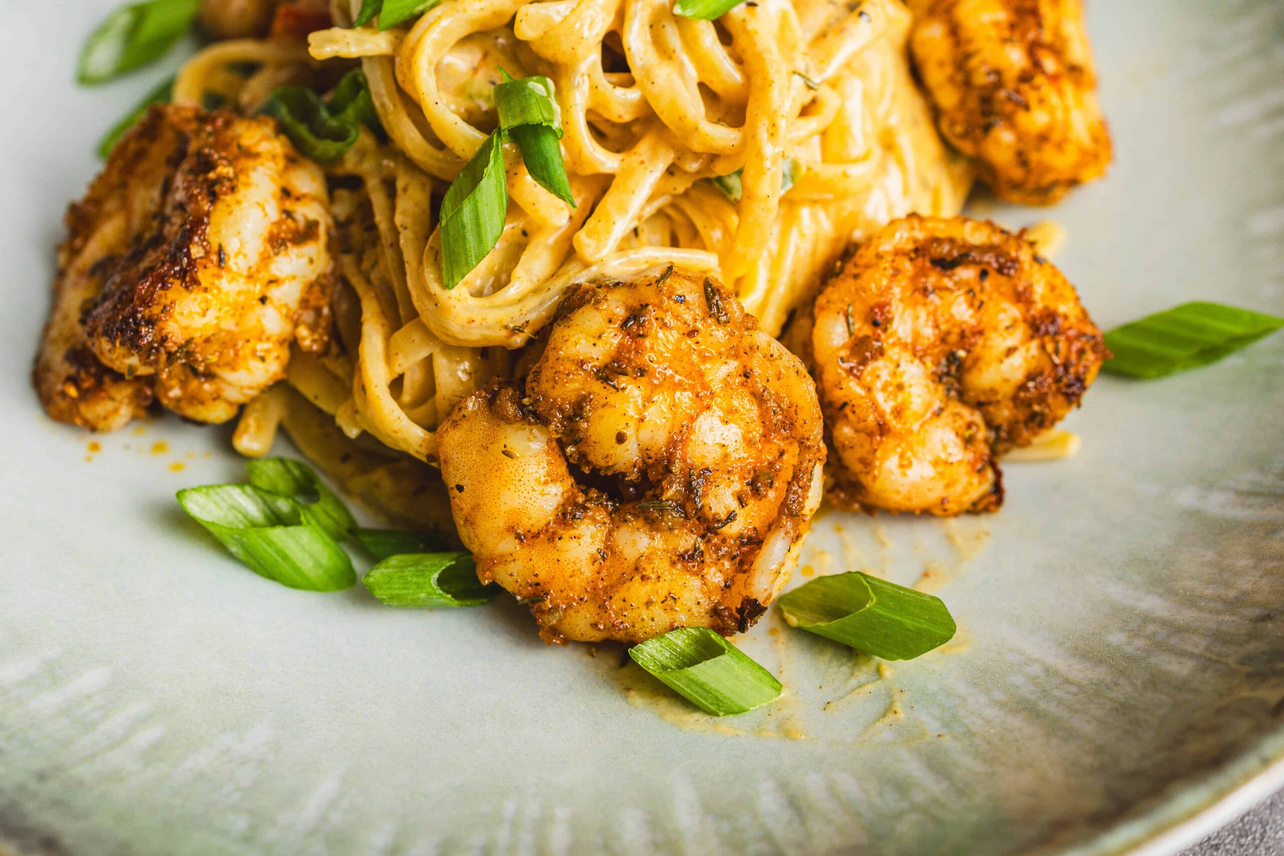 Juicy shrimp with spicy seasoning served with creamy pasta and garnished with chopped green onions, creating a delicious seafood pasta dish perfect for dinner.