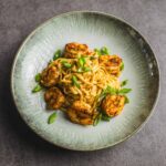 Succulent shrimp and creamy pasta dish garnished with chopped green onions served on a rustic green ceramic plate, perfect for a flavorful seafood meal.