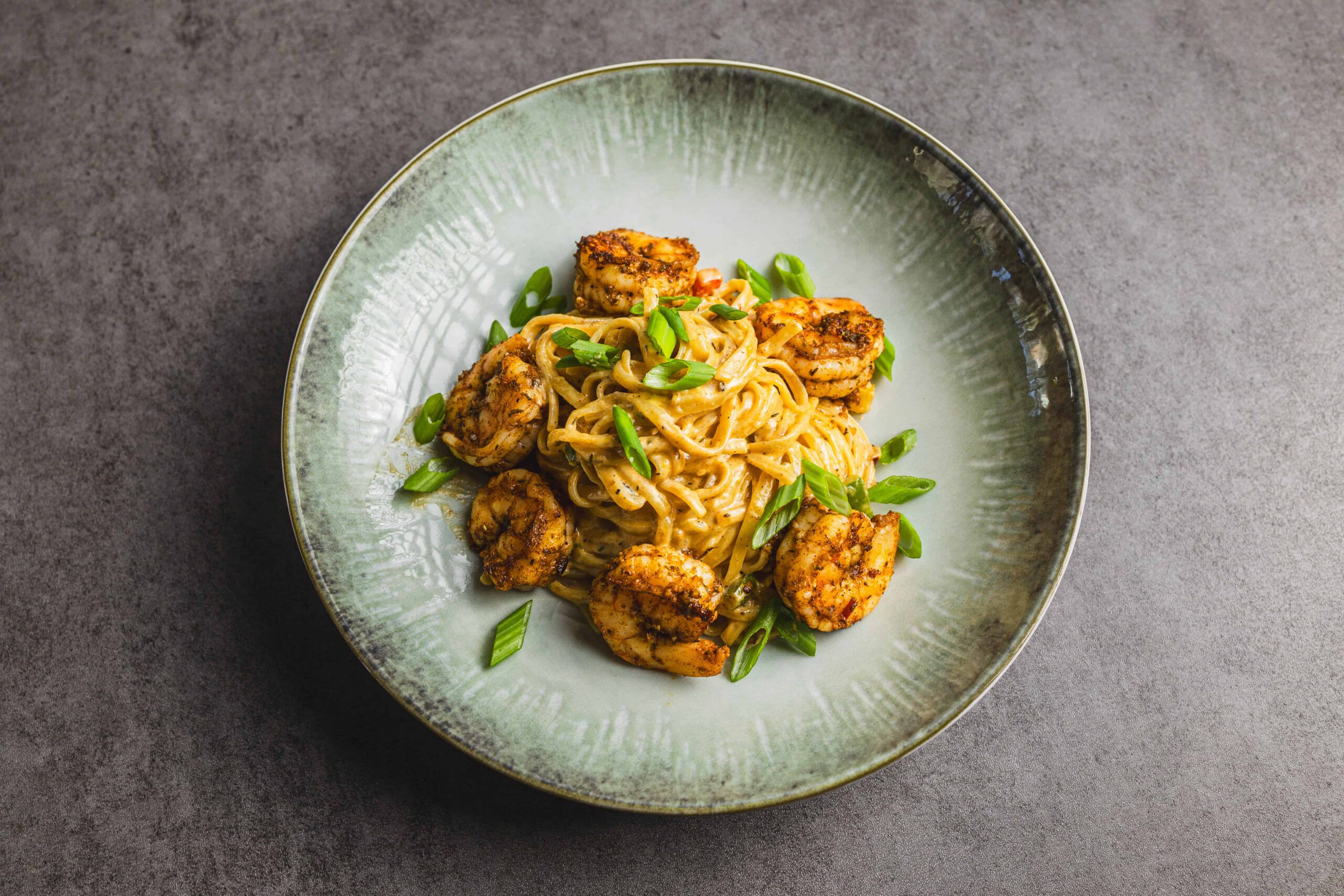 Succulent shrimp and creamy pasta dish garnished with chopped green onions served on a rustic green ceramic plate, perfect for a flavorful seafood meal.
