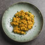 Savory mashed lentils garnished with chopped parsley served on a green ceramic plate.