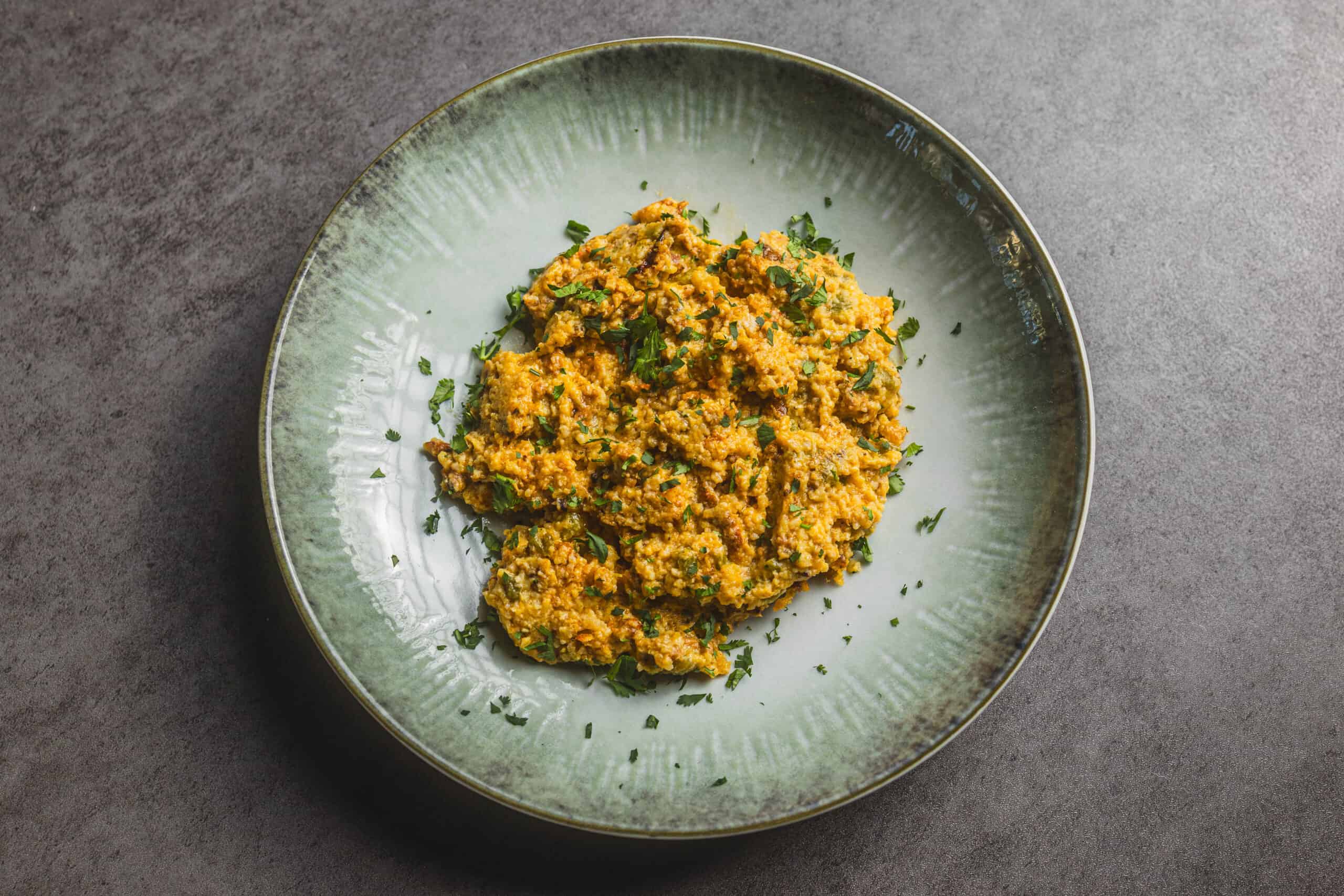 Savory mashed lentils garnished with chopped parsley served on a green ceramic plate.