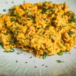 Creamy scrambled eggs with vegetables garnished with chopped cilantro, served on a light-colored plate. Perfect for breakfast or brunch, healthy and flavorful egg scramble with herbs and vegetables.