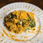 Golden baked spinach casserole with crispy breadcrumb topping on white plate, served as a healthy vegan comfort food dish.