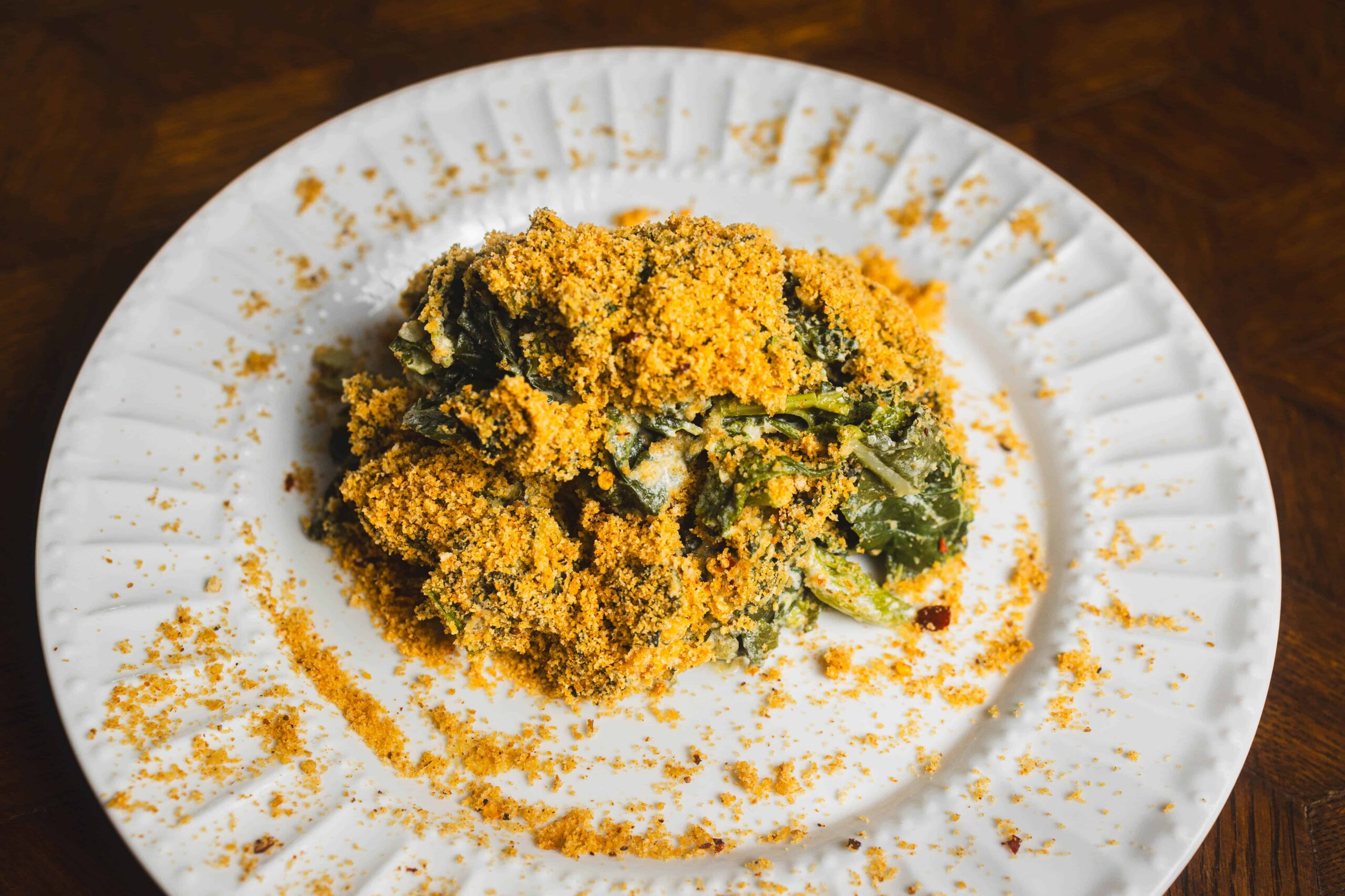 Golden baked spinach casserole with crispy breadcrumb topping on white plate, served as a healthy vegan comfort food dish.