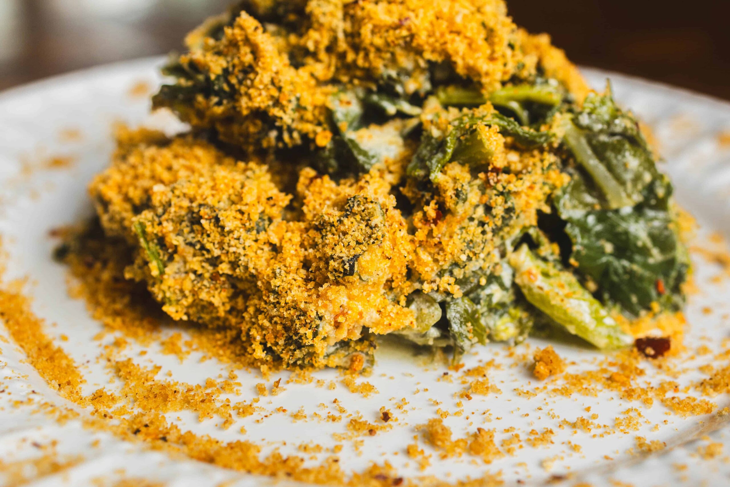 Crispy fried spinach with golden breading on white plate, healthy vegetarian appetizer, close-up of crunchy spinach leaves coated in seasoned breadcrumbs, perfect for a nutritious snack or side dish.