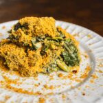 Crunchy baked vegetable casserole with a golden breadcrumb topping served on a white ceramic plate, garnished with fresh greens and seasoned with herbs.