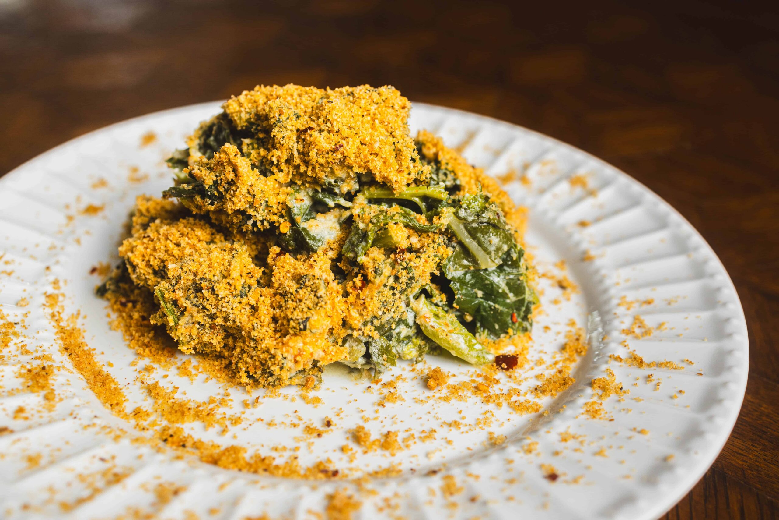 Crunchy baked vegetable casserole with a golden breadcrumb topping served on a white ceramic plate, garnished with fresh greens and seasoned with herbs.