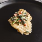 Roasted fish fillet topped with creamy vegetable sauce on black plate, gourmet seafood dish, healthy meal, restaurant style presentation, fresh ingredients, close-up, high quality, culinary image, Hey Recipe.