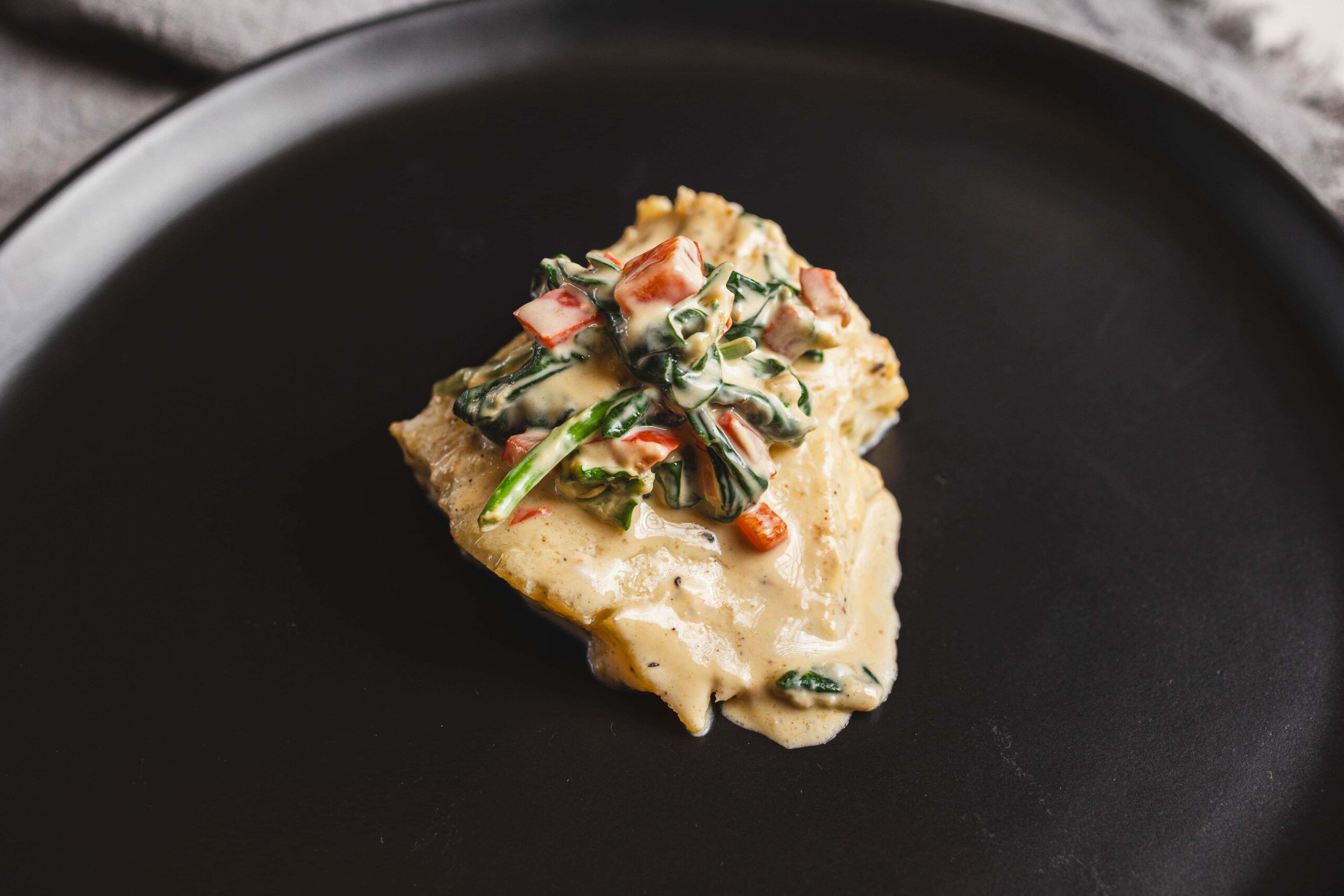 Roasted fish fillet topped with creamy vegetable sauce on black plate, gourmet seafood dish, healthy meal, restaurant style presentation, fresh ingredients, close-up, high quality, culinary image, Hey Recipe.
