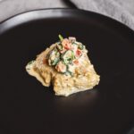 Creamy baked potato topped with fresh vegetable salad on a black plate, perfect for comfort food or dinner recipes.