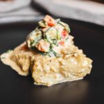 Creamy fish pie topped with fresh vegetable salad on black plate, savory seafood dish with cheese and herbs, elegant presentation of fish and vegetables, restaurant-quality seafood recipe, comfortable home-cooked meal, perfect for dinner or special occasions.