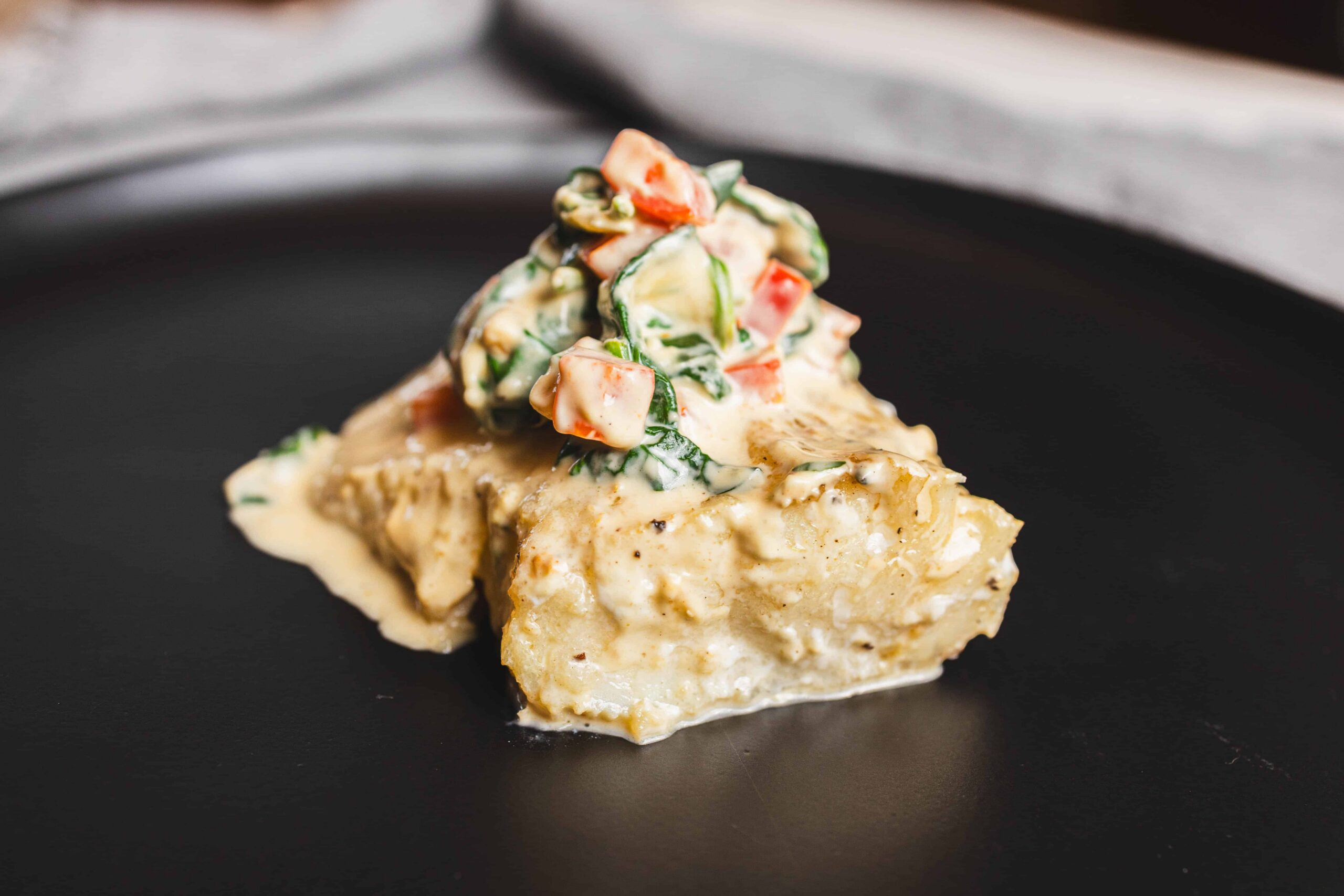 Creamy fish pie topped with fresh vegetable salad on black plate, savory seafood dish with cheese and herbs, elegant presentation of fish and vegetables, restaurant-quality seafood recipe, comfortable home-cooked meal, perfect for dinner or special occasions.
