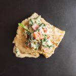 Creamy crab salad on a crispy tortilla chip with mayonnaise and fresh herbs, served on a black plate, perfect for appetizer or snack, popular in seafood cuisine.